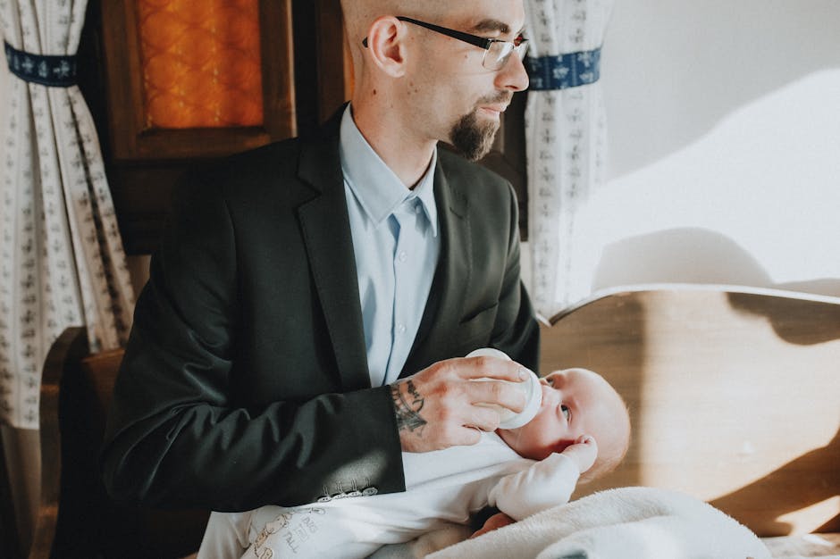 A father in a suit bottle-feeding his baby in a warmly lit room, symbolizing care and bonding.